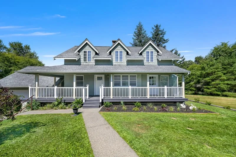 Sage-green home with three dormers, a covered front porch and a lawn